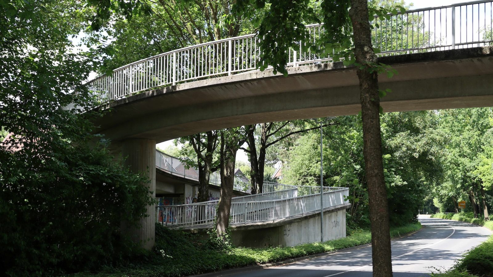 Betonbrücke mit weißem Geländer für Fußgänger und Radfahrer über eine baumgesäumte Straße in Coesfeld