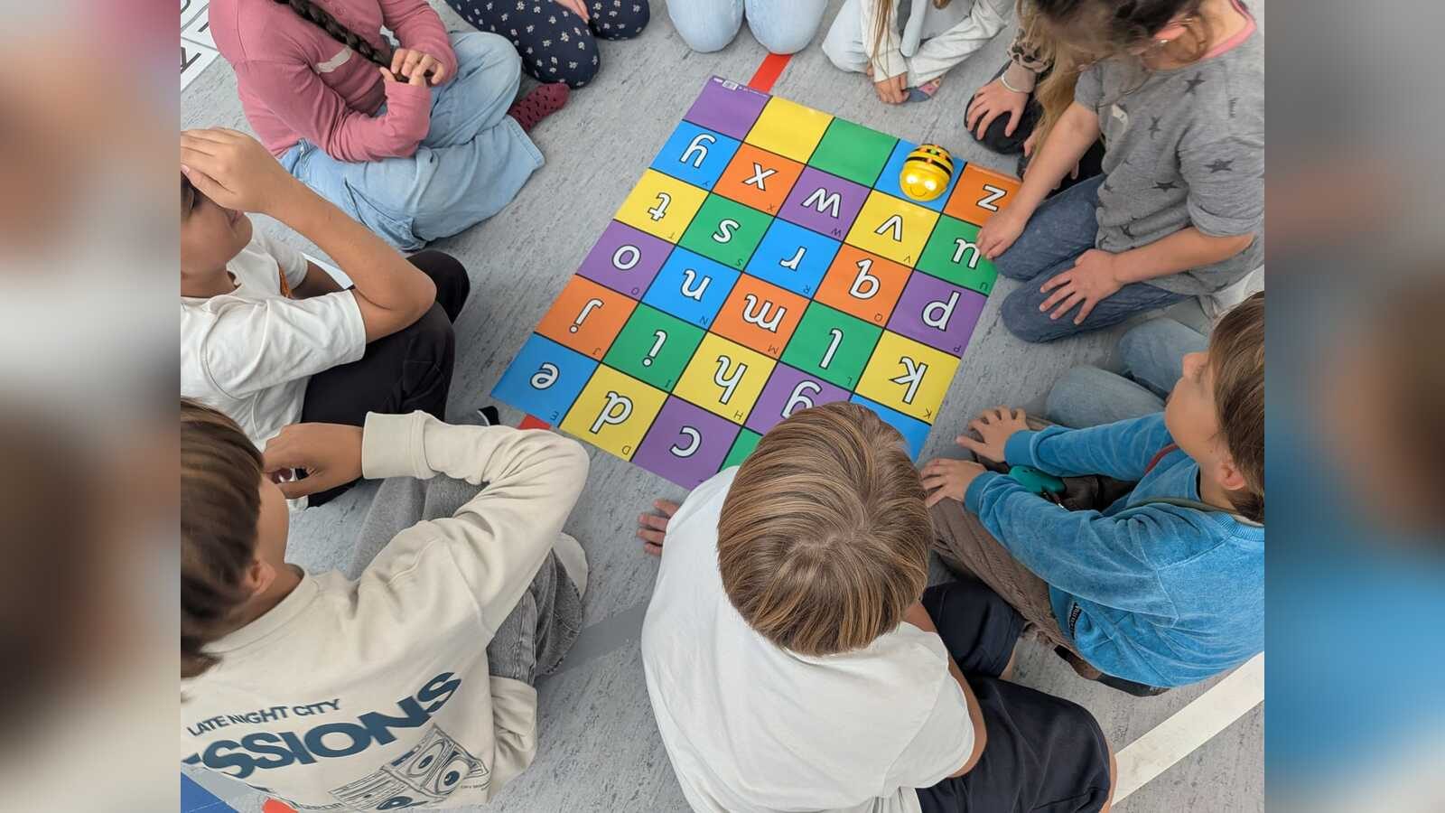 Grundschulkinder programmieren einen Lernroboter auf einer Buchstabenmatte
