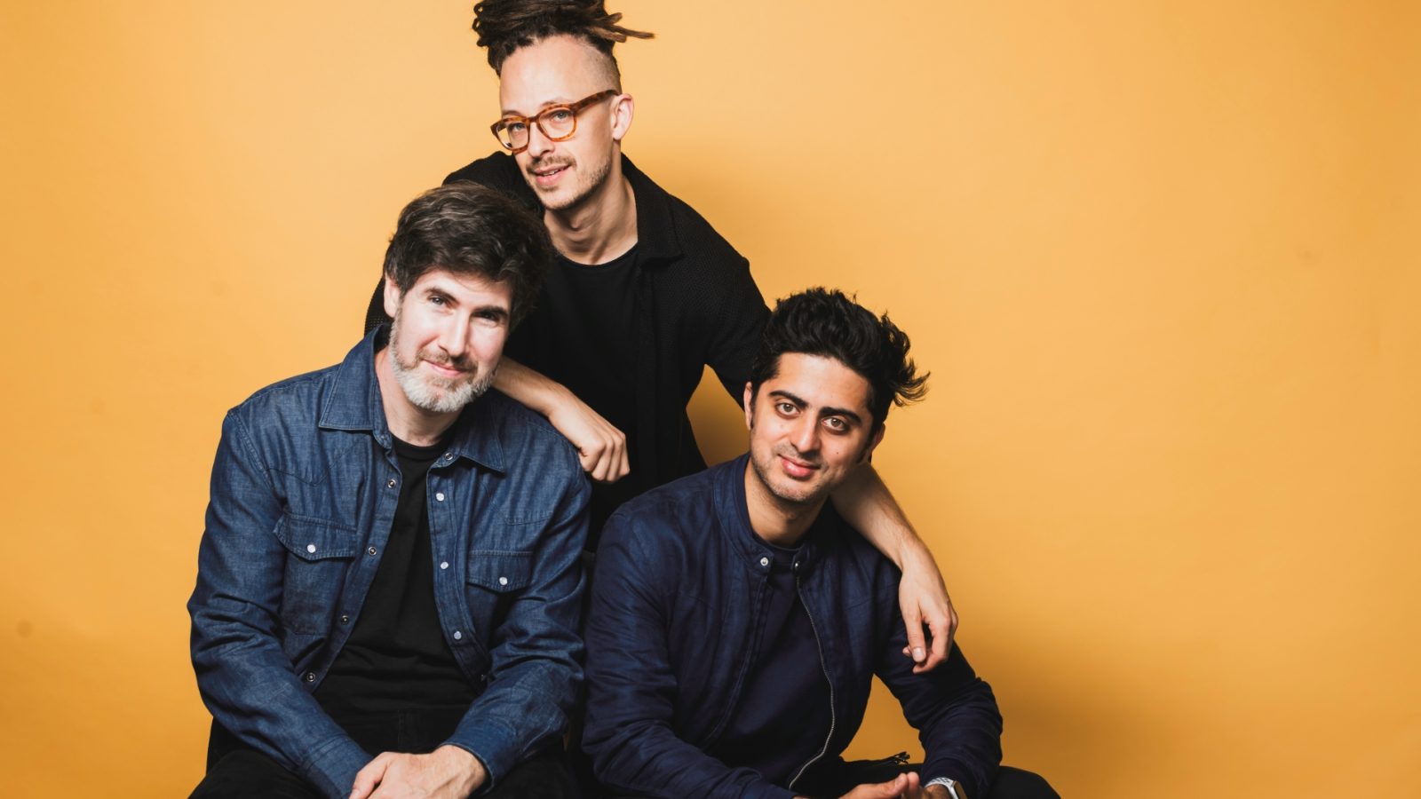 Philippe Lemm Trio mit drei Mitgliedern vor einem gelben Hintergrund, lächelnd und in lässiger Kleidung.