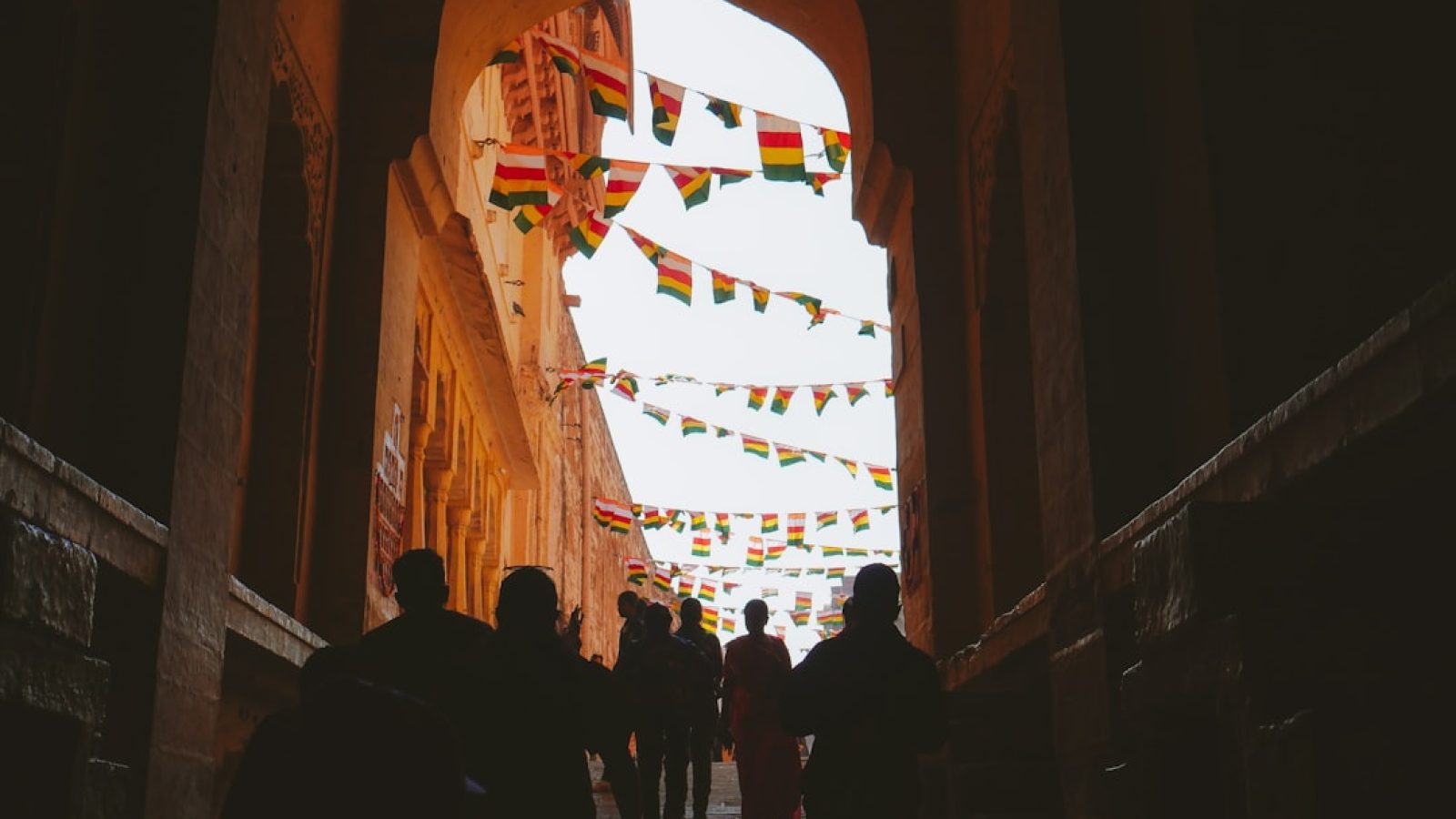 Menschen gehen durch einen Torbogen, umgeben von bunten Fahnen in einem historischen Gebäude.