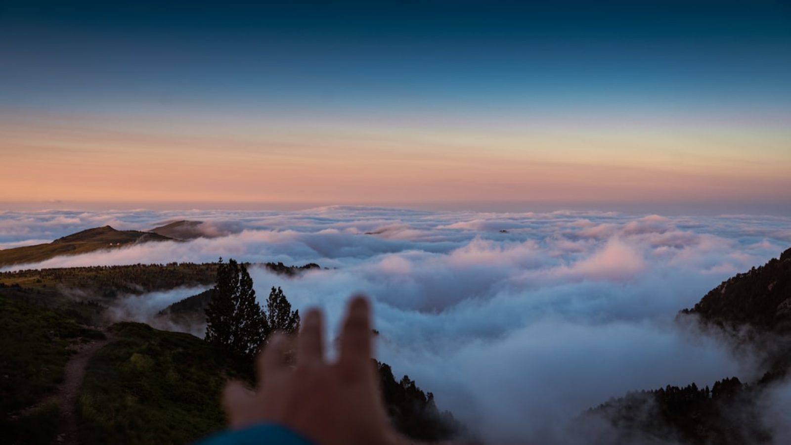Hand, die auf eine Wolkendecke blickt, mit einem klaren Himmel im Hintergrund während der Dämmerung.