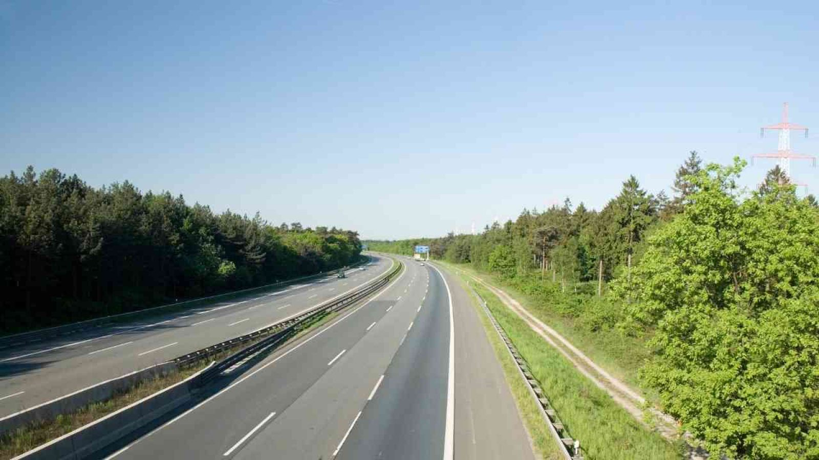 Leere Autobahn mit zwei Fahrspuren und grünen Bäumen entlang der Seite in einer klaren Umgebung.