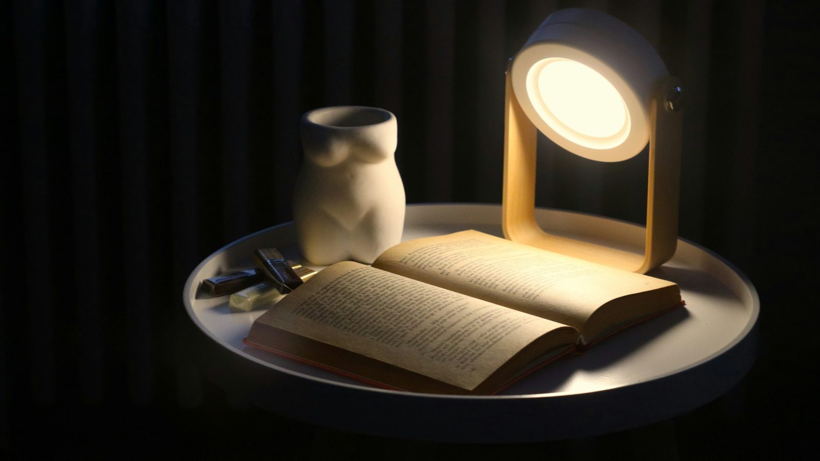 Ein aufgeschlagenes Buch liegt neben einer Lampe auf einem Tisch