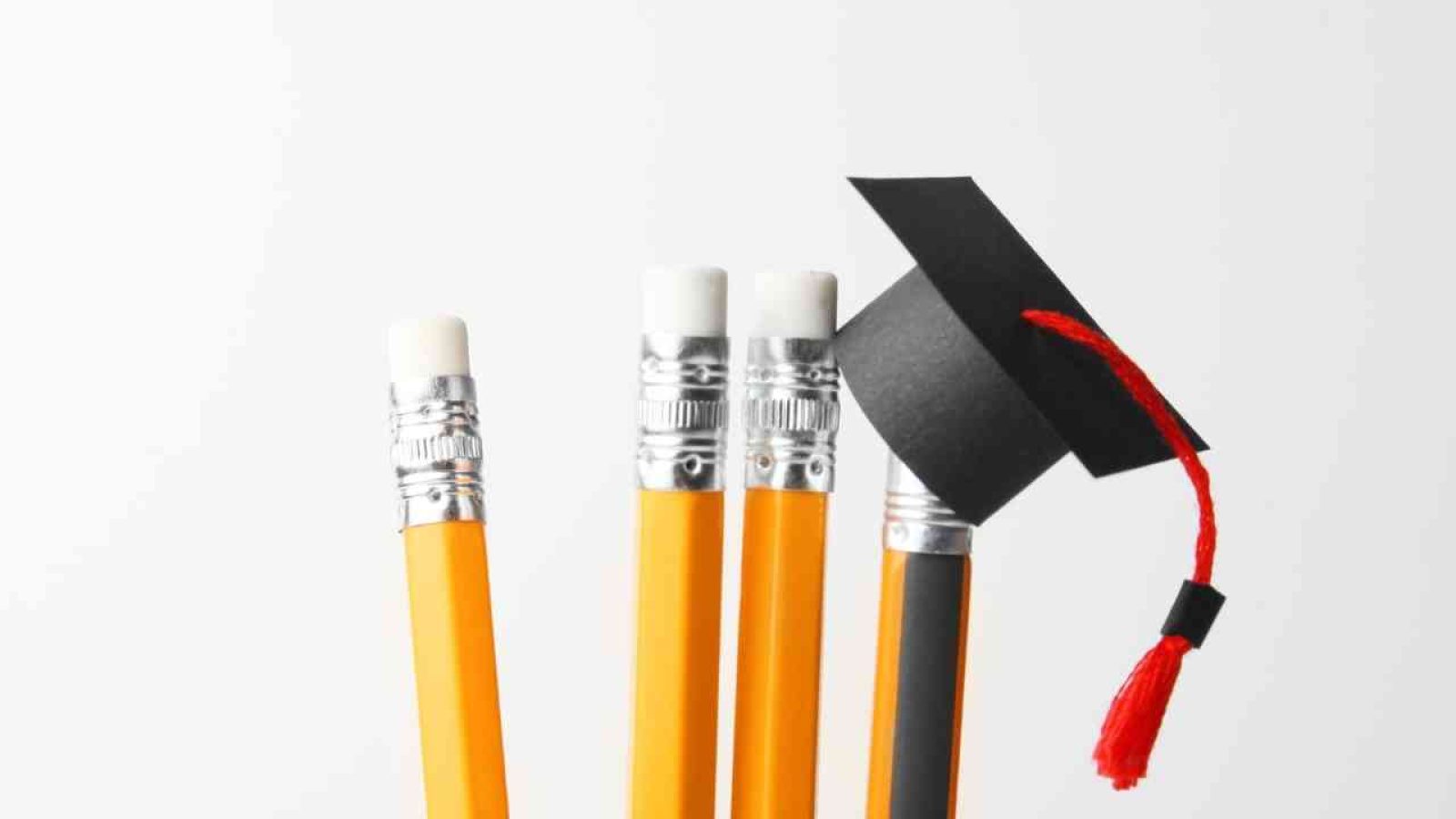 Vier gelbe Bleistifte mit Radiergummis und ein schwarzer Abschlusshut mit rotem Quast.