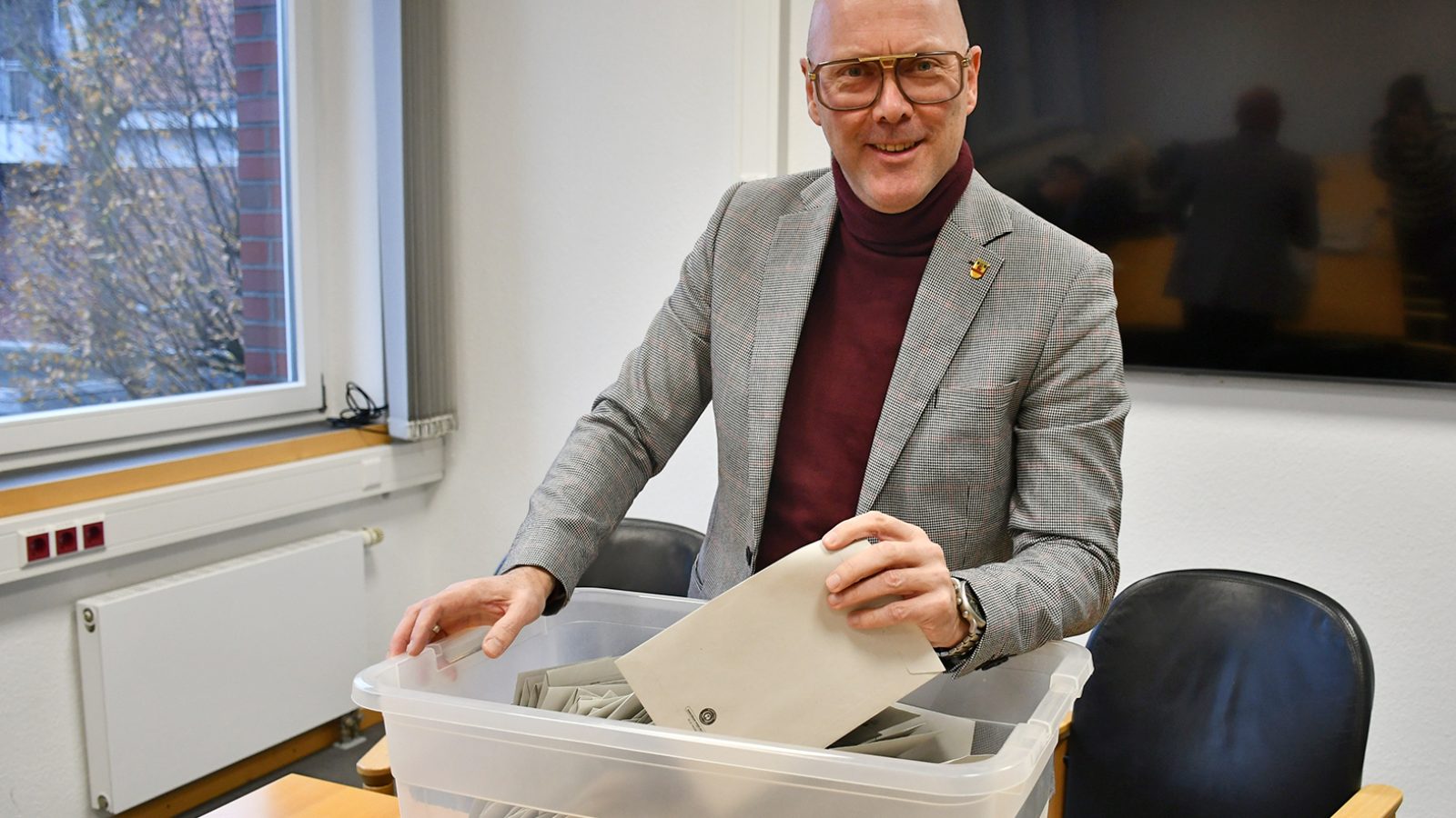 Mann mit Brille in grauem Anzug, der Umschläge aus einer durchsichtigen Box entnimmt.