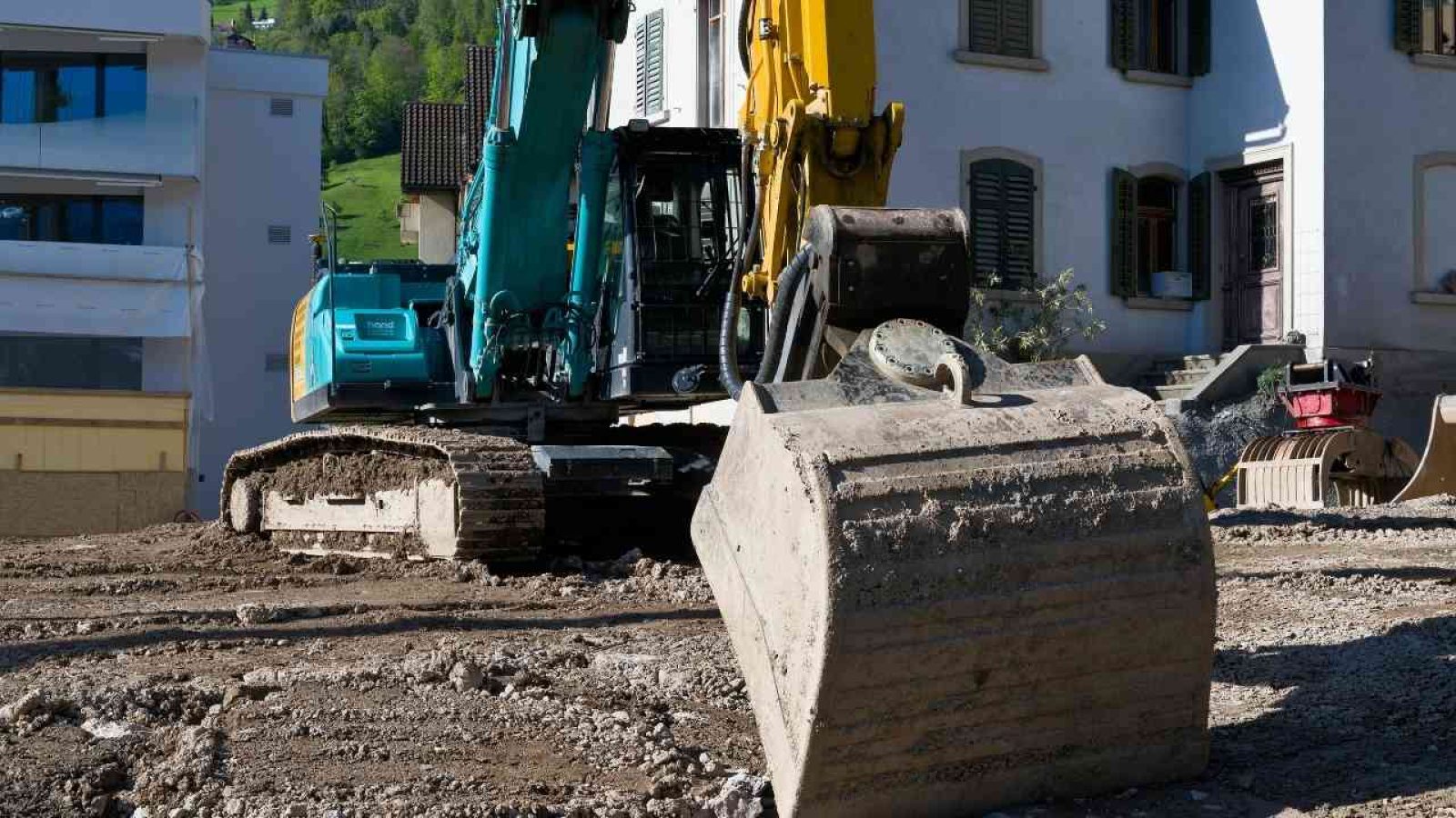 Bagger auf Baustelle vor Gebäuden im Sonnenlicht, bereit für Erdarbeiten und Bauprojekte.