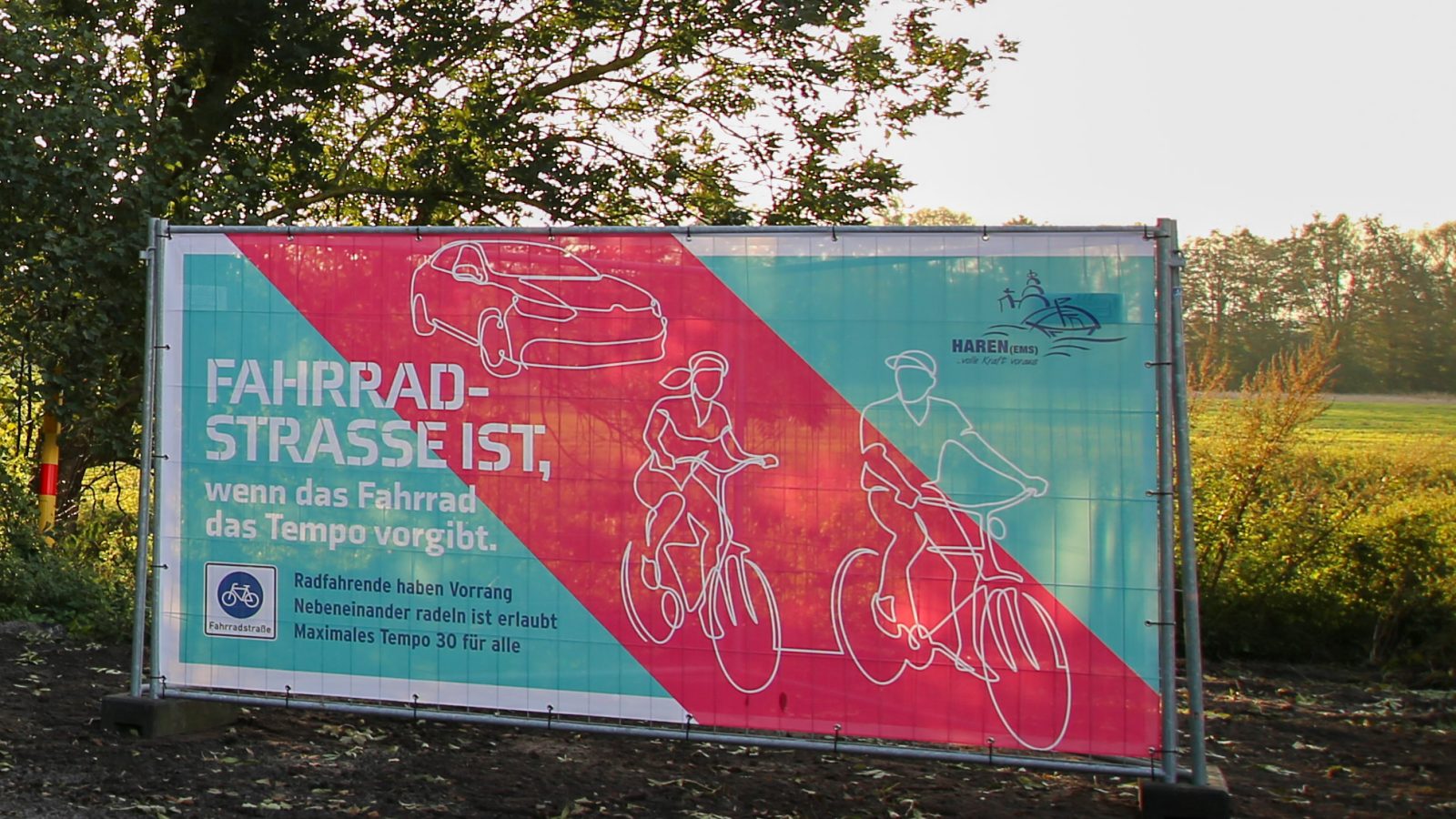 Zwei Bauzaunbanner entlang der Fahrradstraße weisen auf die wichtigsten Verkehrsregelungen einer Fahrradstraße hin. Vor allem, dass das Rad das Tempo vorgibt.
