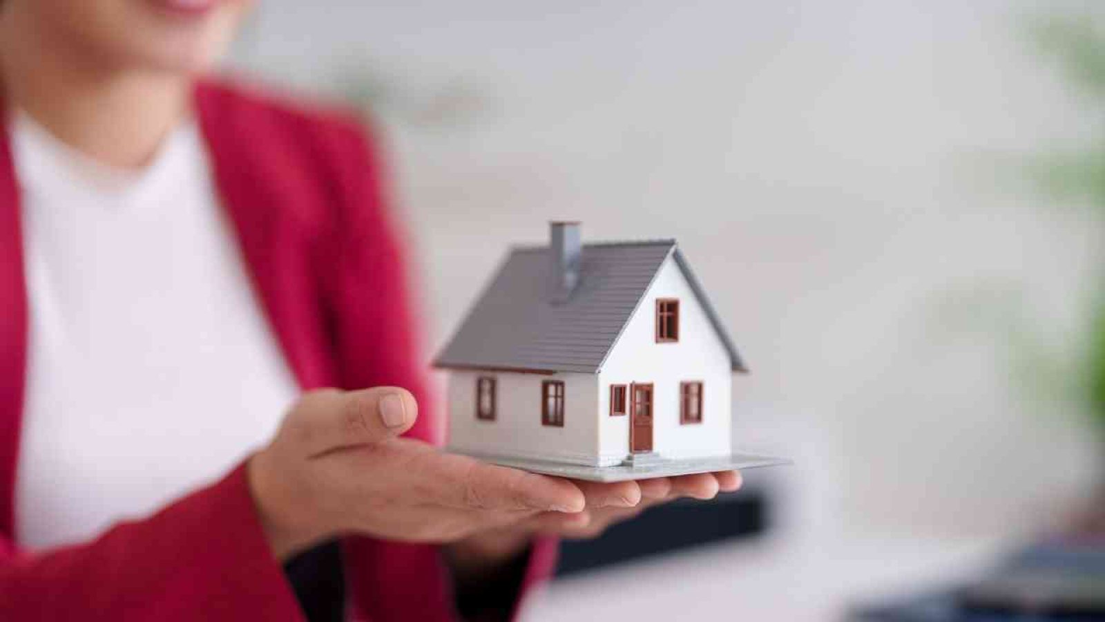 Eine Person hält ein kleines Modell eines Hauses in der Hand, das Details wie Fenster und Tür zeigt.