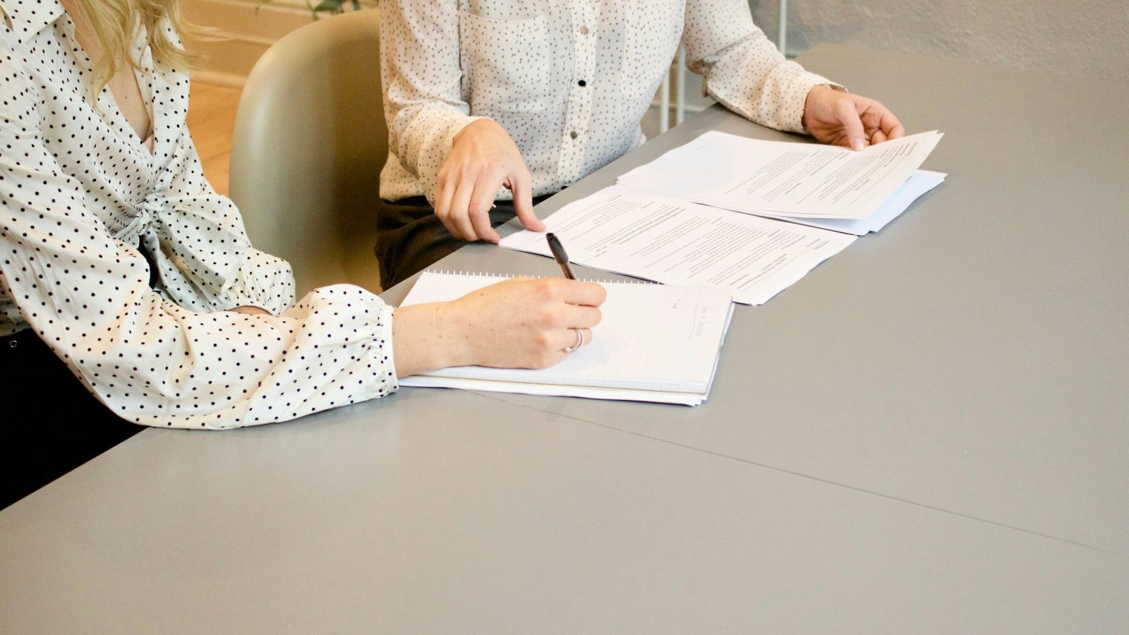Zwei Frauen am Tisch, eine unterschreibt ein Dokument