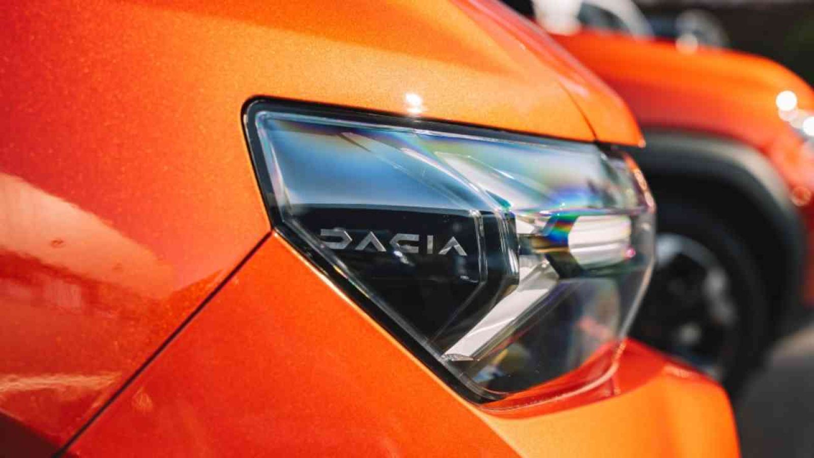 Nahaufnahme des Scheinwerfers eines orangefarbenen Fahrzeugs mit dem Schriftzug 'Dacia'.