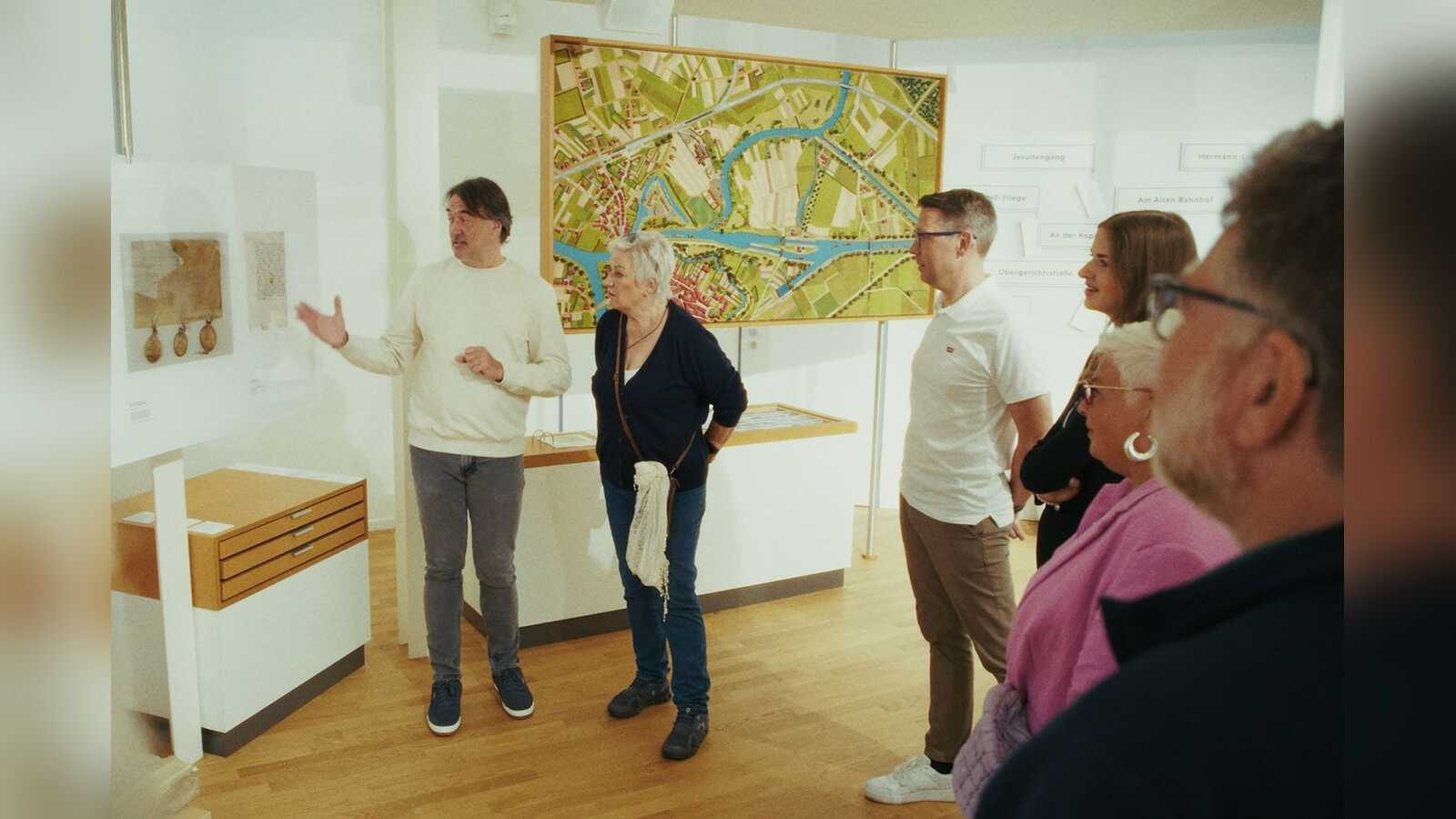 Museumsführer erklärt einer Besuchergruppe historische Urkunden, im Hintergrund ein großes Stadtmodell von Meppen