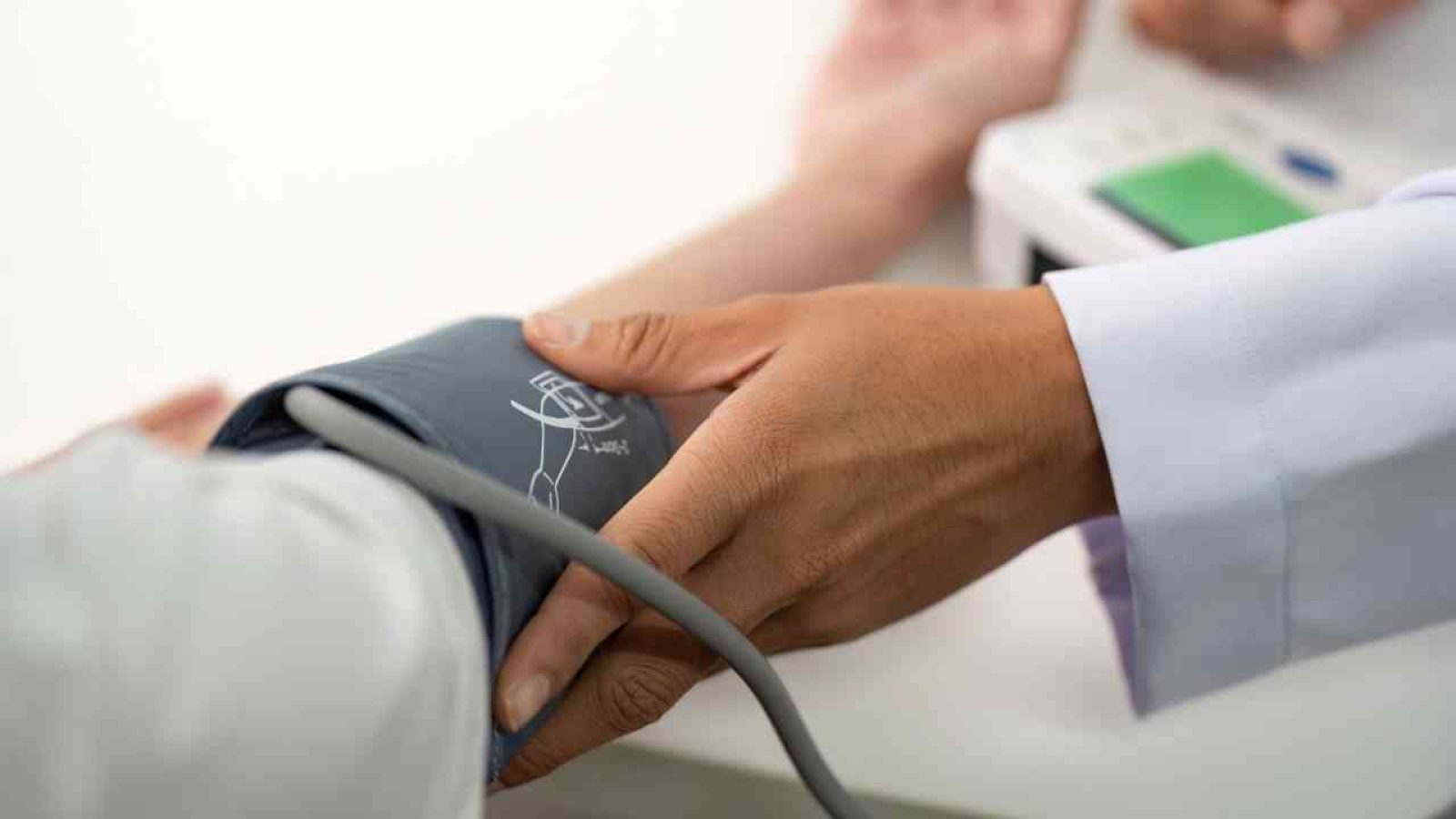 Arzt misst Blutdruck bei Patient mit Manschette und digitalen Messgerät im Gesundheitswesen.