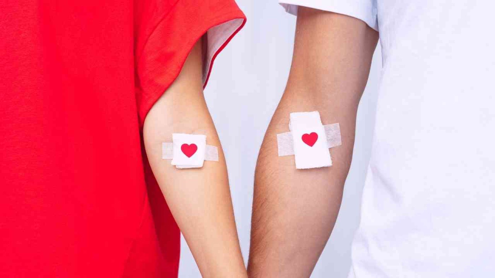 Zwei Arme mit Pflastern und Herzsymbolen, symbolisieren Blutspende und Solidarität in Rot und Weiß.