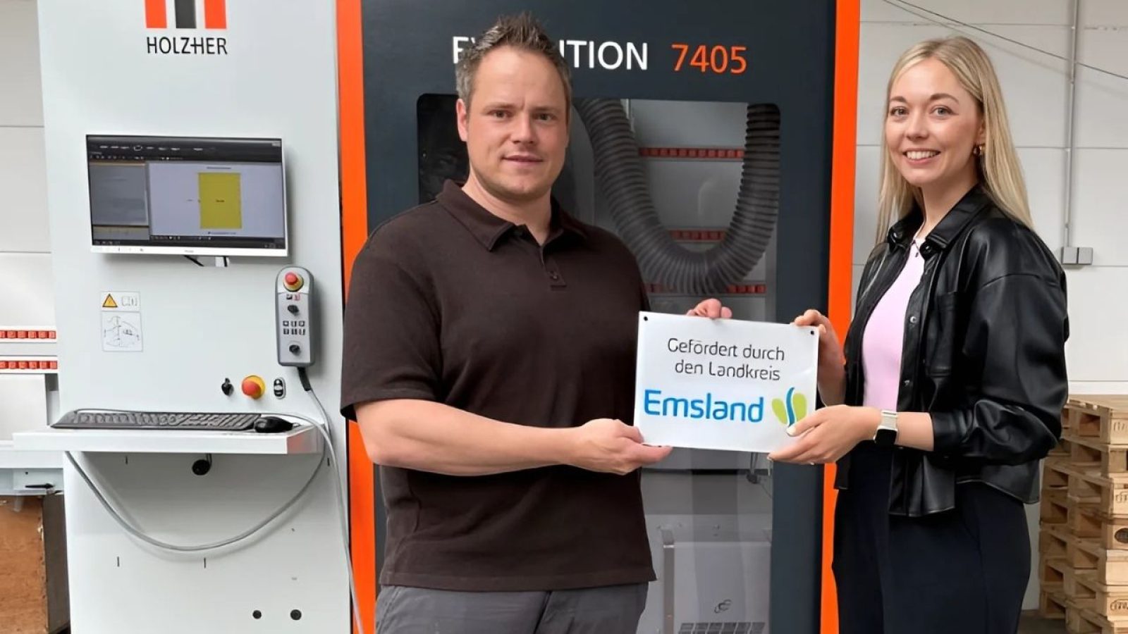 Mann und Frau präsentieren Emsland-Förderung vor HOLZHER Evolution 7405 Maschine in einem industriellen Umfeld.