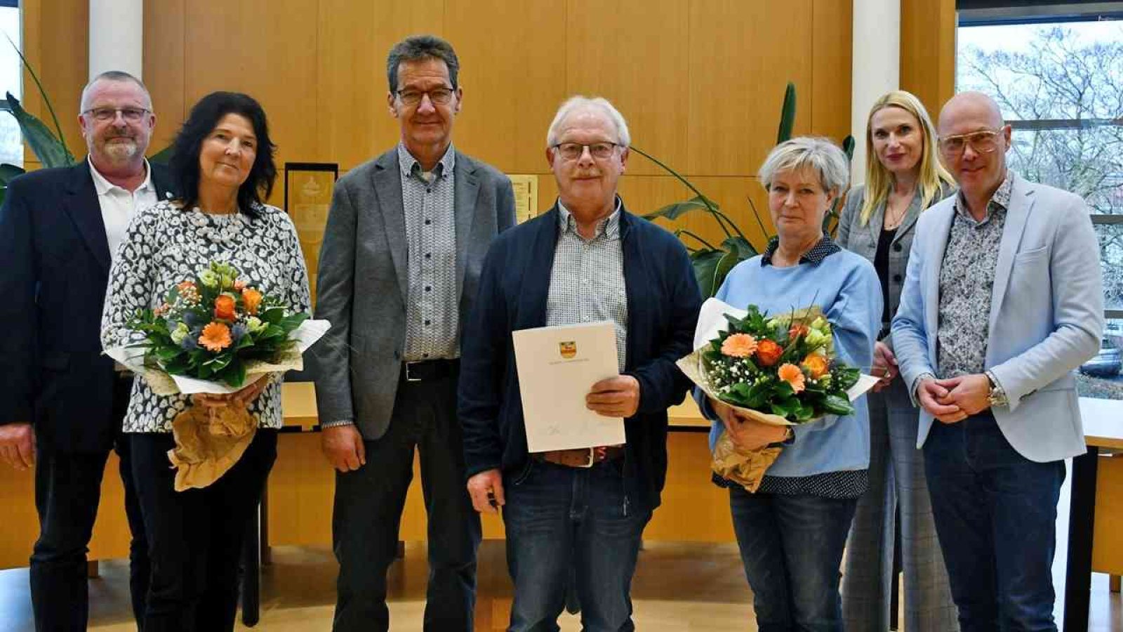 Gruppe von Personen mit Blumensträußen und Urkunde in einem Innenraum bei einer Feierlichkeit in Cloppenburg.