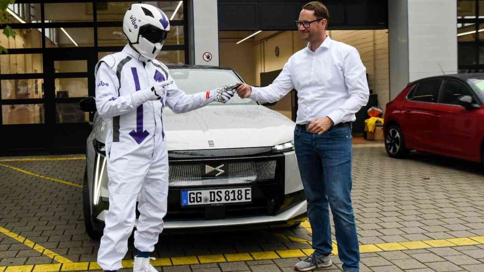 Ein Mann gibt einem Rennfahrer einen Schlüssel vor einem weißen Auto weiter, Symbol für Autokauf oder Fahrzeugübergabe.