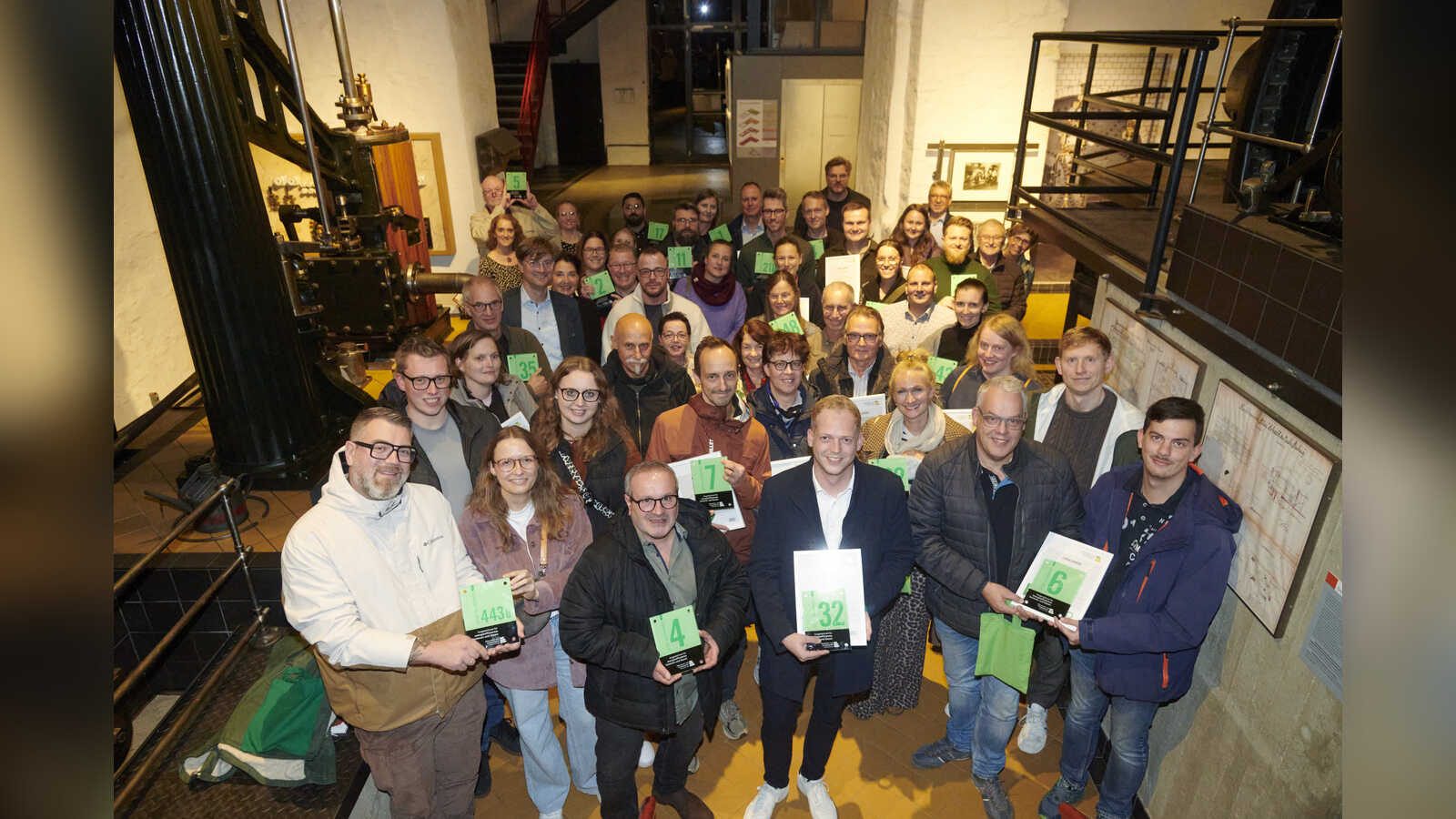 Gruppenfoto der ausgezeichneten Hauseigentümerinnen und Hauseigentümer mit ihren Grünen Hausnummern im Museum Industriekultur Osnabrück