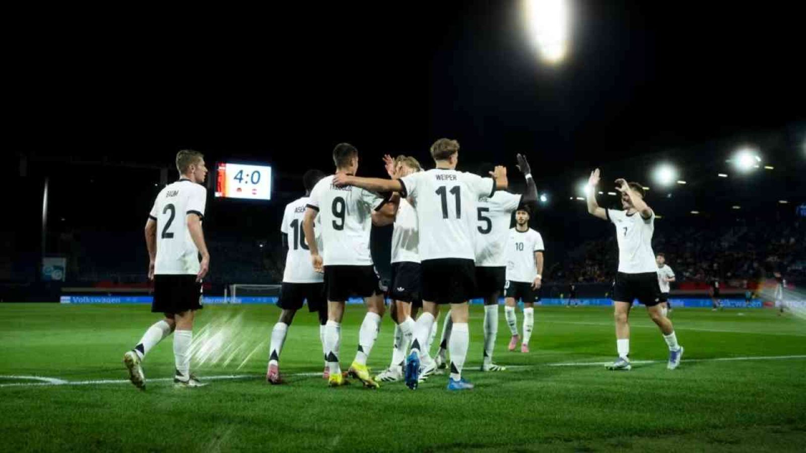 Eine Fußballmannschaft in weißen Trikots feiert ein Tor während eines Spiels im Stadion.