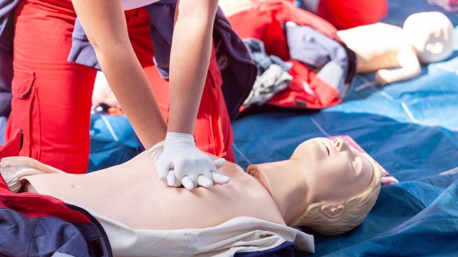 Erste-Hilfe-Training: Person übt Herz-Lungen-Wiederbelebung an einer Puppe, Fokus auf Hände in Aktion.