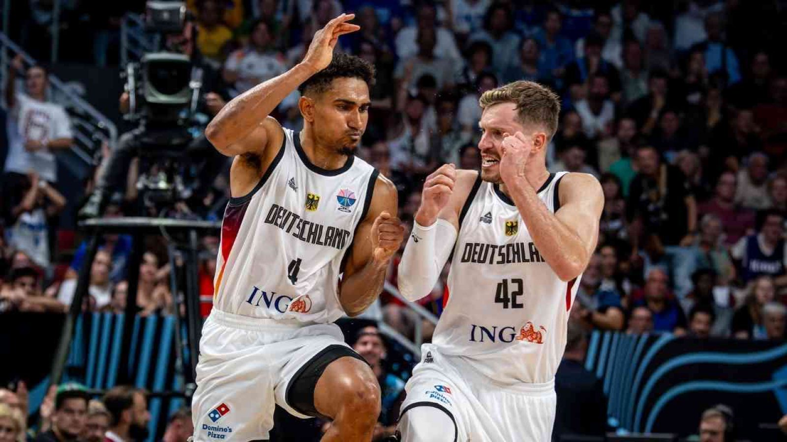 Basketballspieler im Deutschland-Trikot feiern auf dem Feld vor jubelnden Fans bei einem spannenden Spiel.