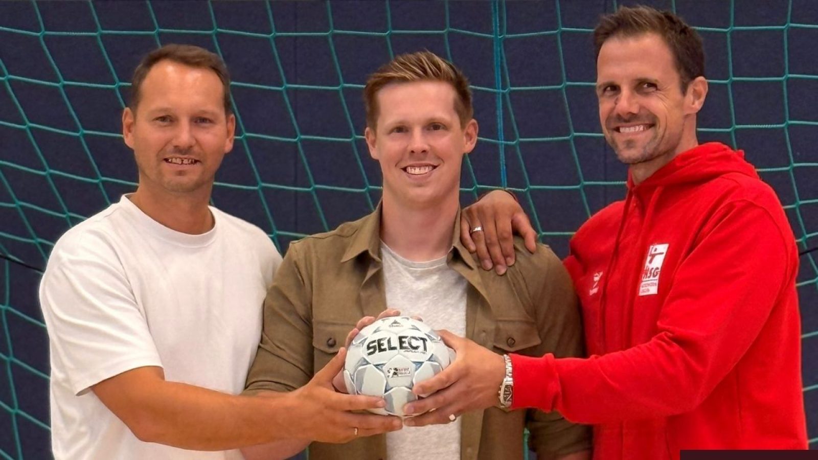 Drei Männer mit Handball vor einem Tor, lächeln in die Kamera, Teamgeist symbolisiert Sport und Gemeinschaft.