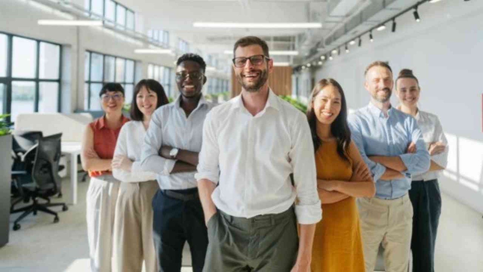 Gruppe von sieben Personen, die in einem modernen Büro lächeln und aufgestellt sind, mit verschiedenen Kleidungsstilen.