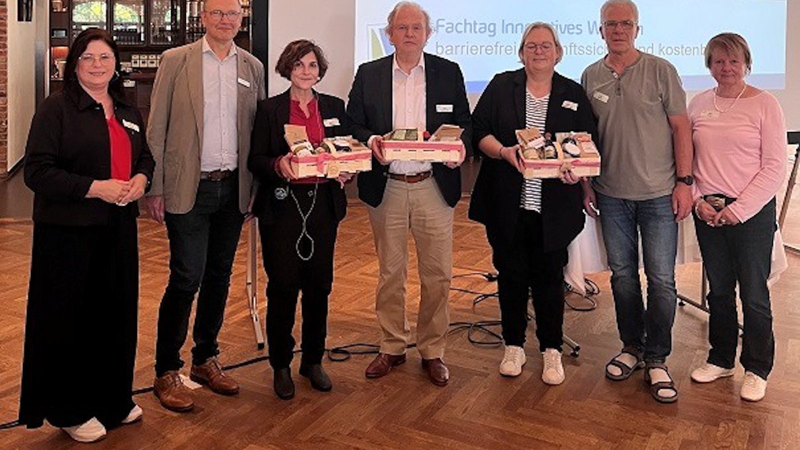 Sieben Personen stehen vor einer Leinwand mit dem Titel des Fachtags Innovatives Wohnen