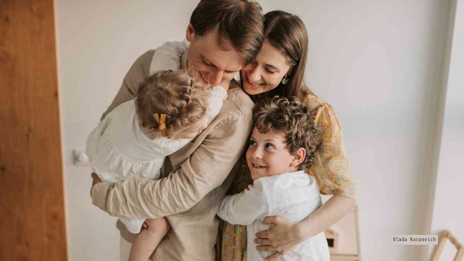 Familie mit zwei Kindern, die in einer Umarmung zusammenstehen, während sie lächeln und Freude ausstrahlen.