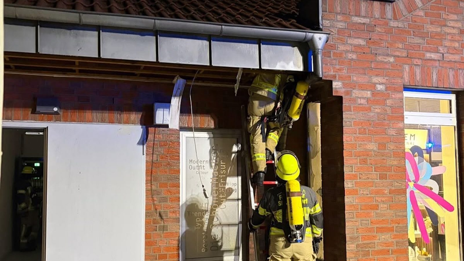 Feuerwehrleute mit Atemschutz auf einer Steigleiter bei der Kontrolle des Gebäudes am Verbrauchermarkt in Schüttorf