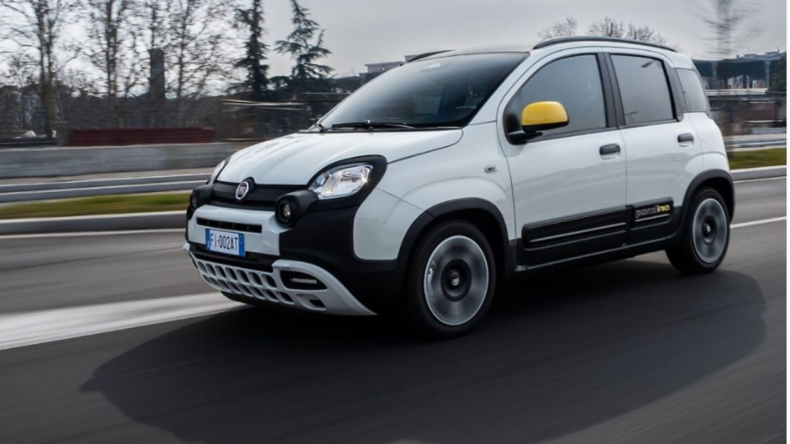 Kompakter weißer Fiat Panda auf einer Straße, mobil und stilvoll, mit gelbem Seitenspiegel.