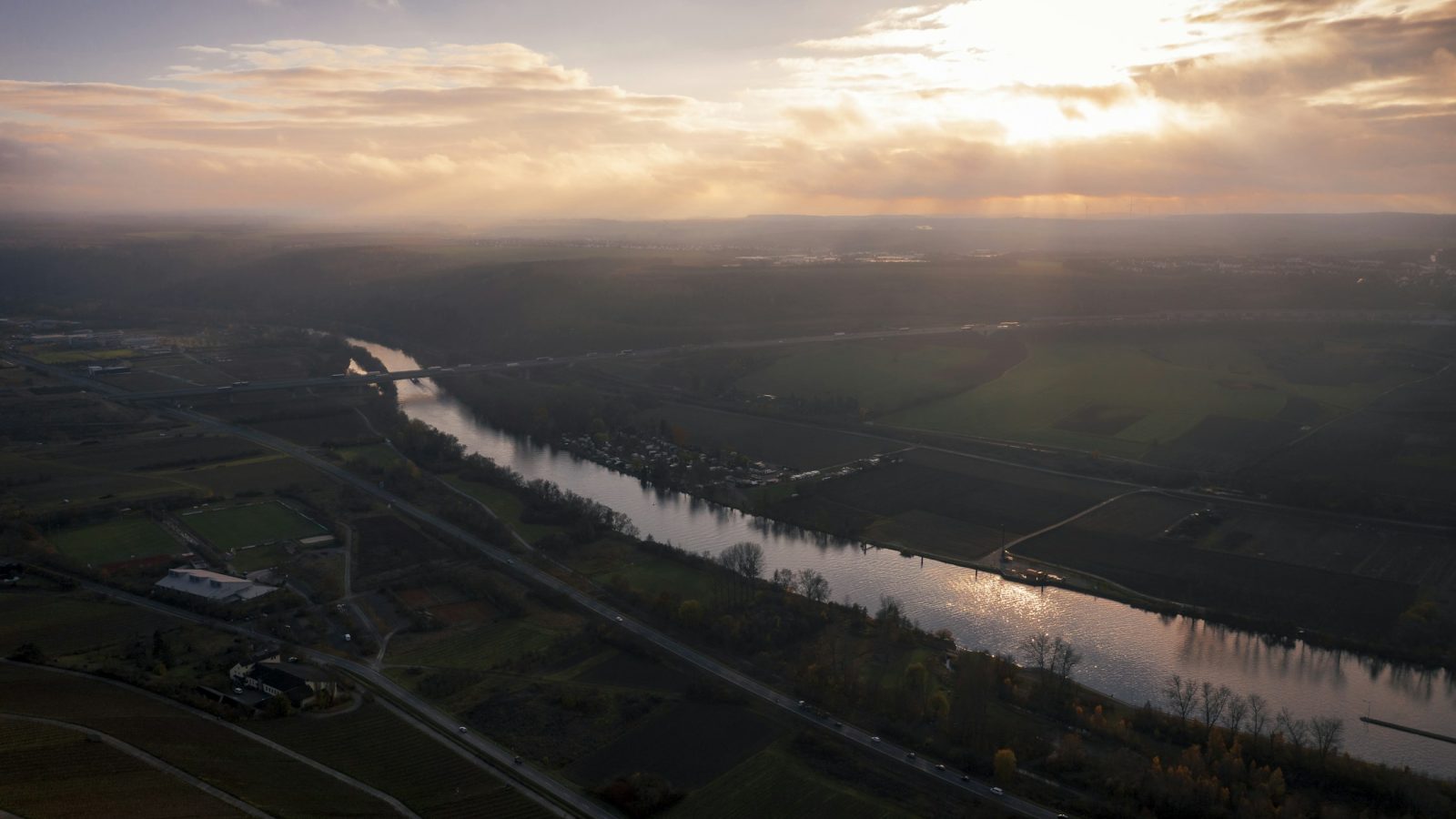 Ein Fluss schlängelt sich unter bewölktem Himmel durch eine grüne, naturnahe Landschaft