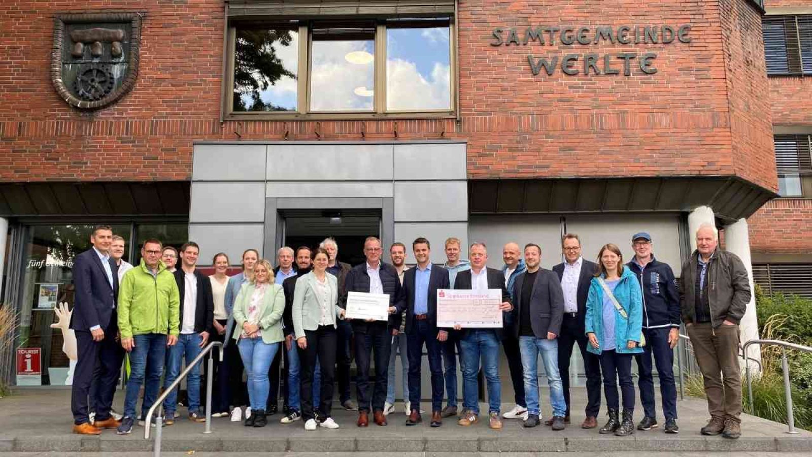 Gruppe von Menschen vor dem Gebäude der Samtgemeinde Werlte, halten Scheck in einem feierlichen Anlass.