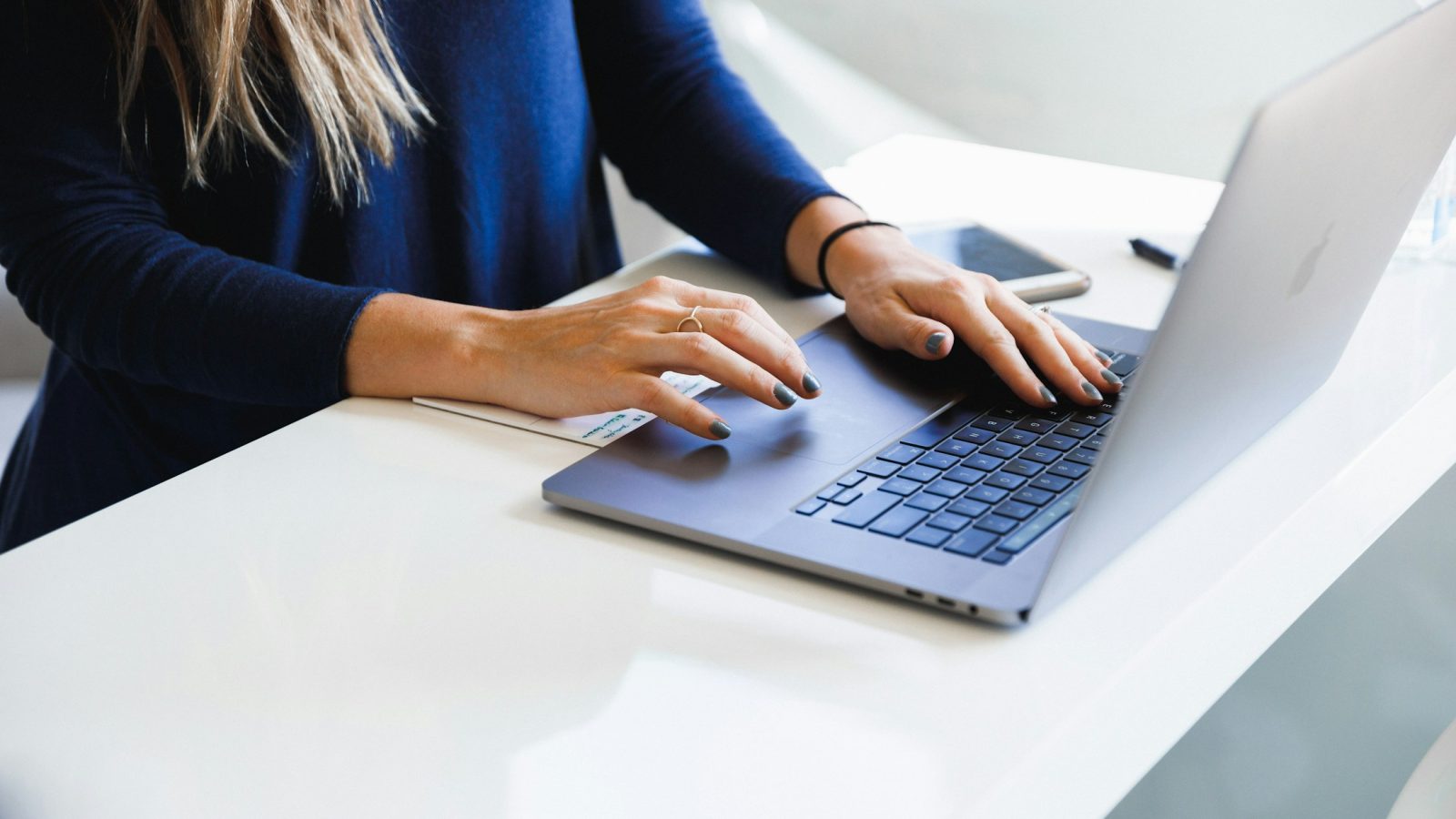 Frau in blauem Oberteil arbeitet an einem Laptop