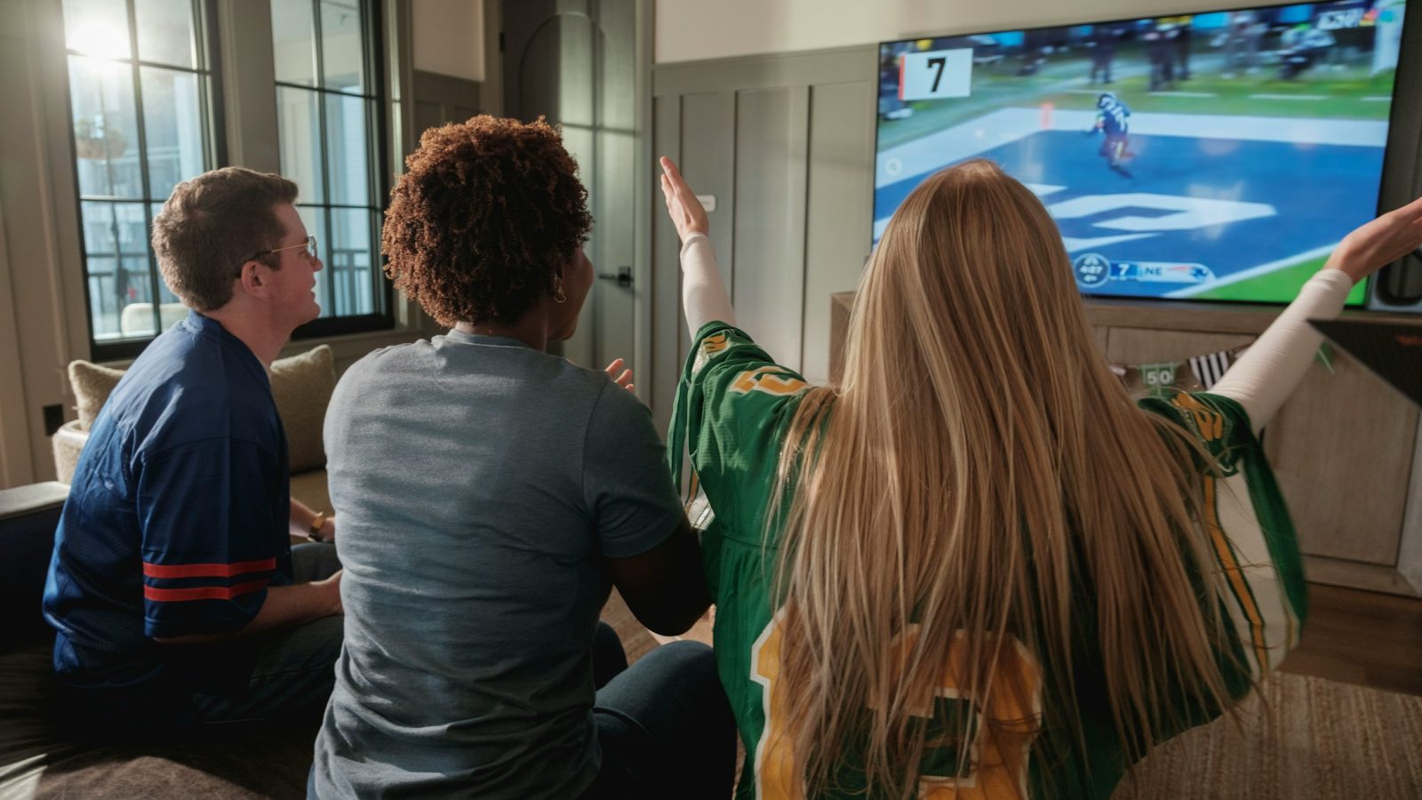 Mehrere Menschen sitzen zusammen vor einem Fernseher und schauen ein Sportspiel