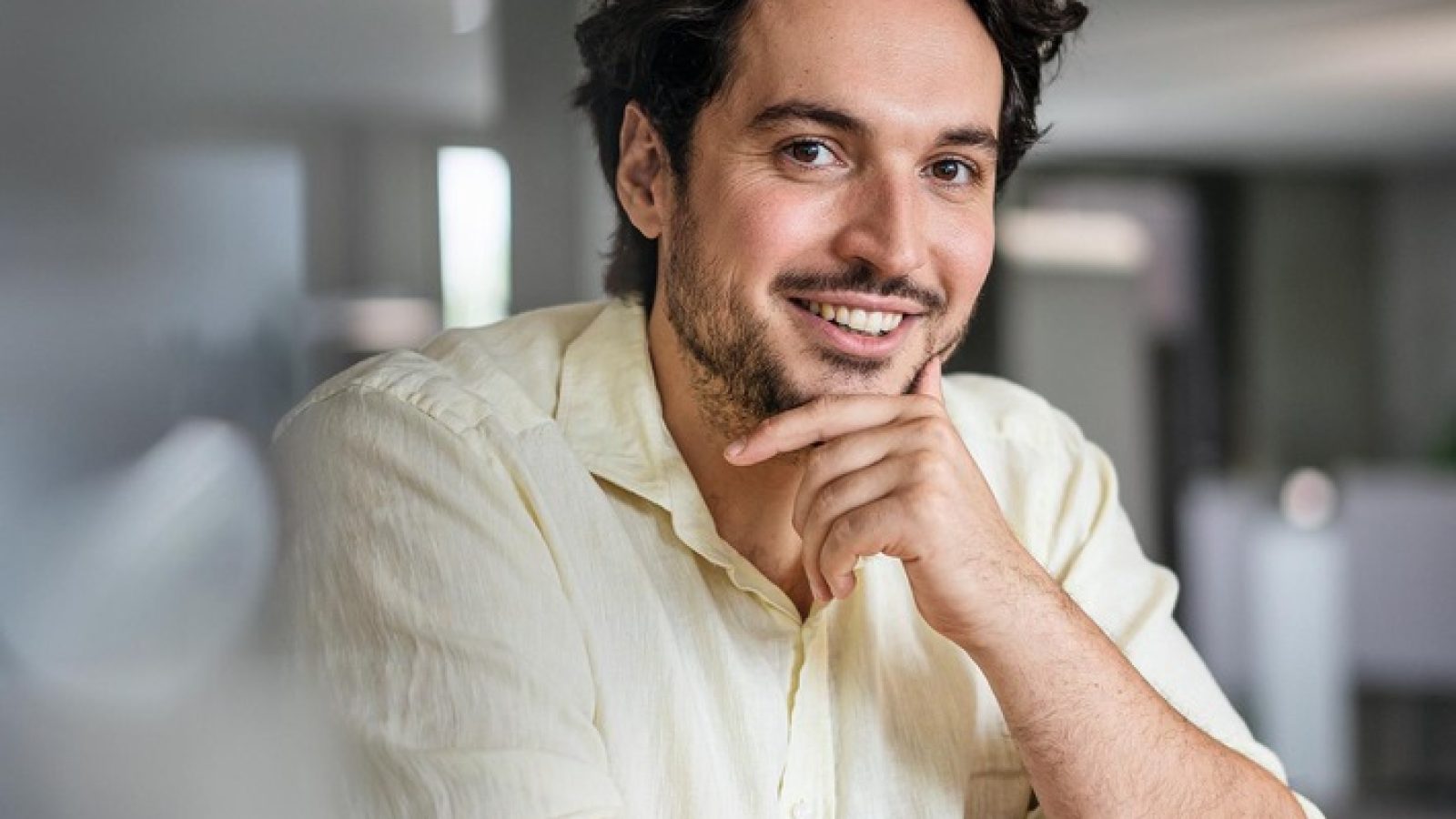Smiling young businessman with hand on chin at office / Weiterer Text über ots und www.presseportal.de/nr/172282 / Die Verwendung dieses Bildes für redaktionelle Zwecke ist unter Beachtung aller mitgeteilten Nutzungsbedingungen zulässig und dann auch honorarfrei. Veröffentlichung ausschließlich mit Bildrechte-Hinweis.