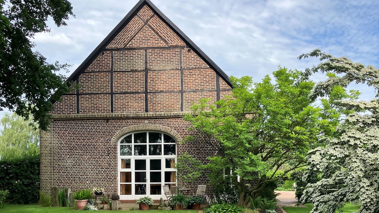 Backsteinhaus mit Fachwerkgiebel und großem Rundbogenfenster hinter einem gepflegten Rasen im Garten Christensen in Lüdinghausen