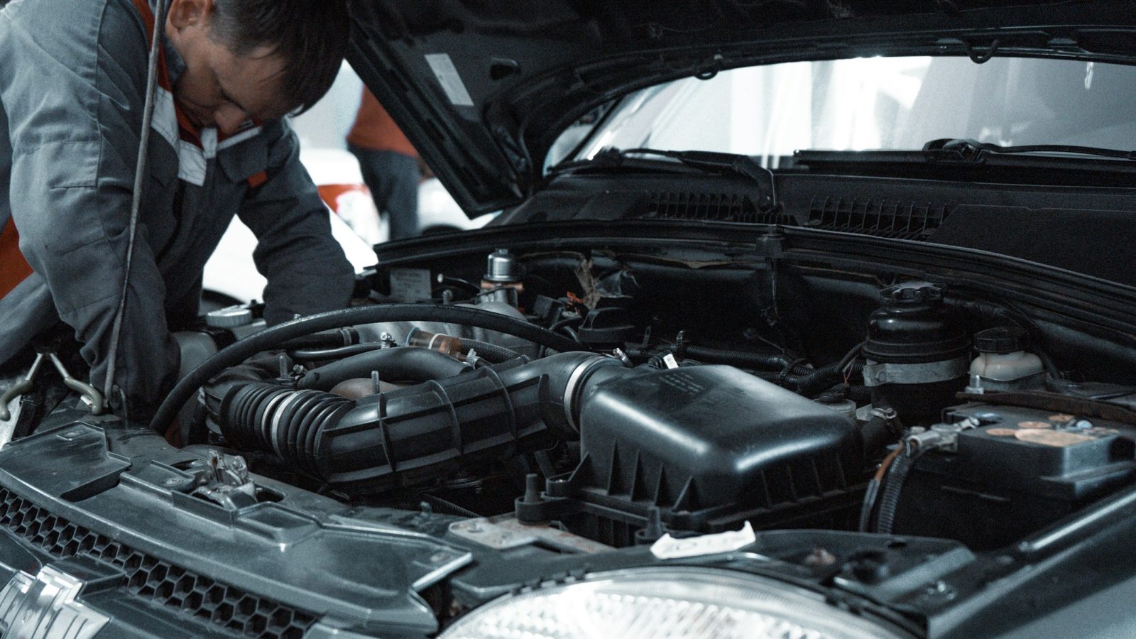 Mechaniker in grauer Arbeitskleidung untersucht den Motor eines Gebrauchtwagens