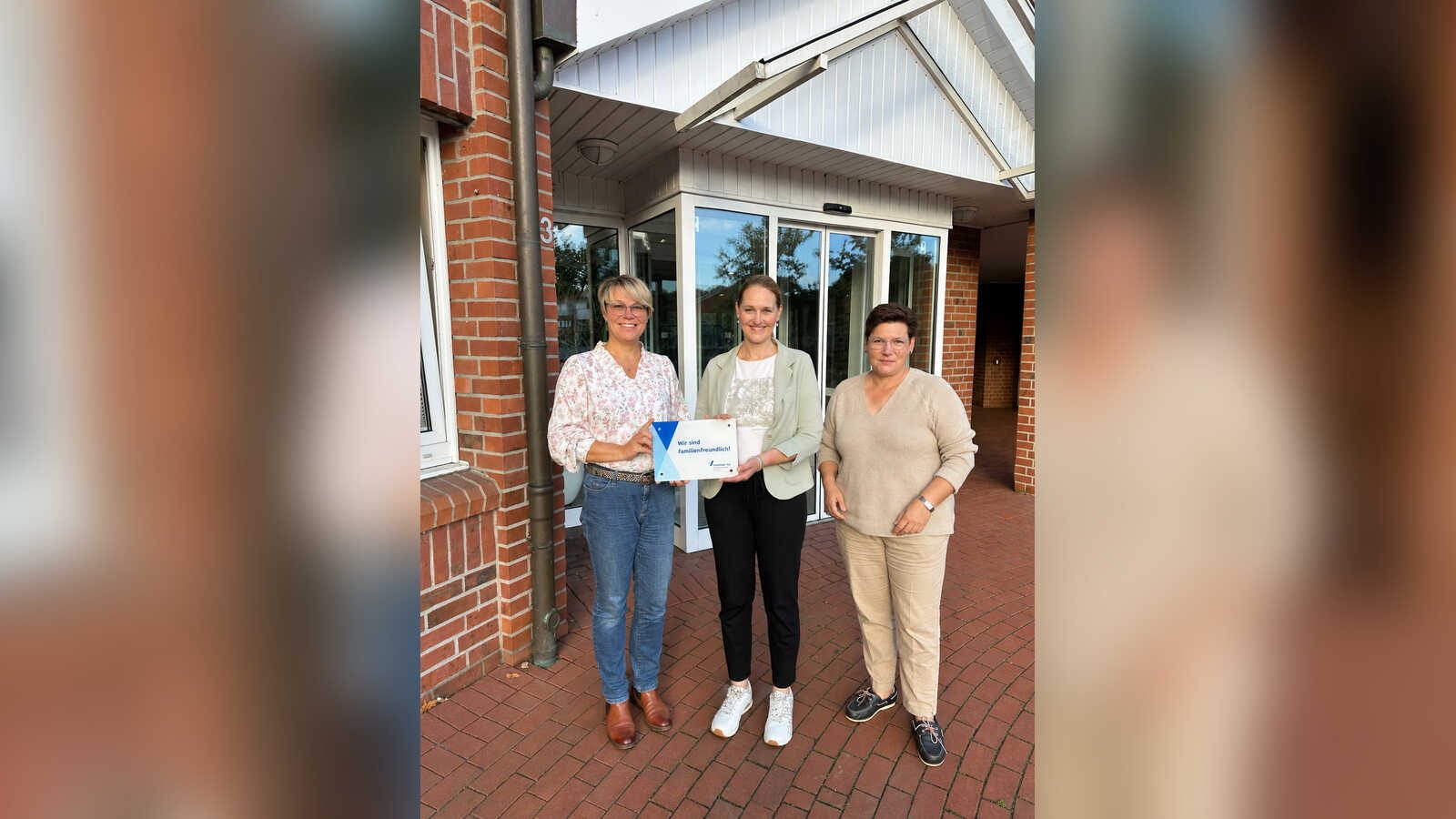 Drei Frauen vor einem Gebäudeeingang, die mittlere hält eine Mitgliedsplakette von vereinbar e.V.