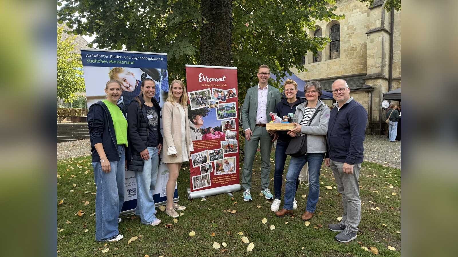 Bürgermeister Carsten Hövekamp übergibt einen Präsentkorb an Hilla Berheide sowie Leonie und Andreas Steens vor dem Banner mit dem prämierten Foto