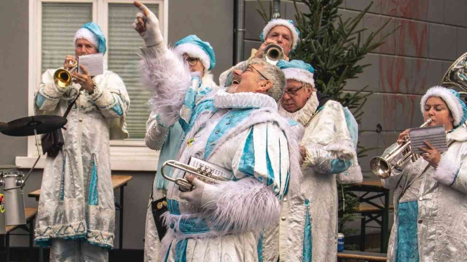 Musiker in festlicher Kleidung mit Trompeten und anderen Instrumenten während einer Aufführung im Freien.