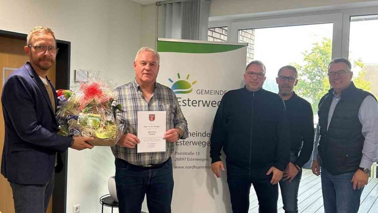 Eine Gruppe von vier Personen, die anlässlich eines Dienstjubiläums zusammenstehen, während einer Person eine Urkunde überreicht wird.