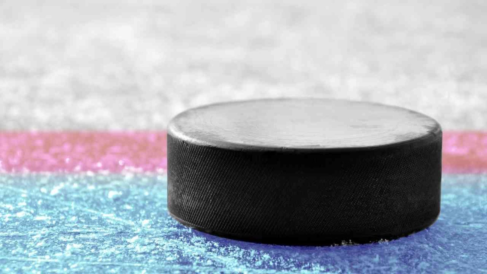 Schwarzer Hockeypuck auf farbigem Eis mit roten und blauen Linien, symbolisiert Spaß und Sport in der Eishalle.