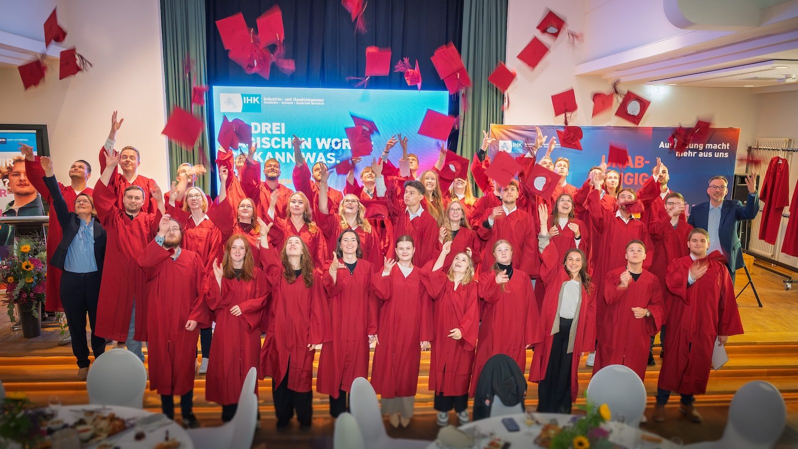 Die IHK-Berufsbesten 2026 in roten Talaren werfen im Saal des Hofbräu an der Wilhelmshöhe in Lingen ihre Absolventenhüte in die Luft