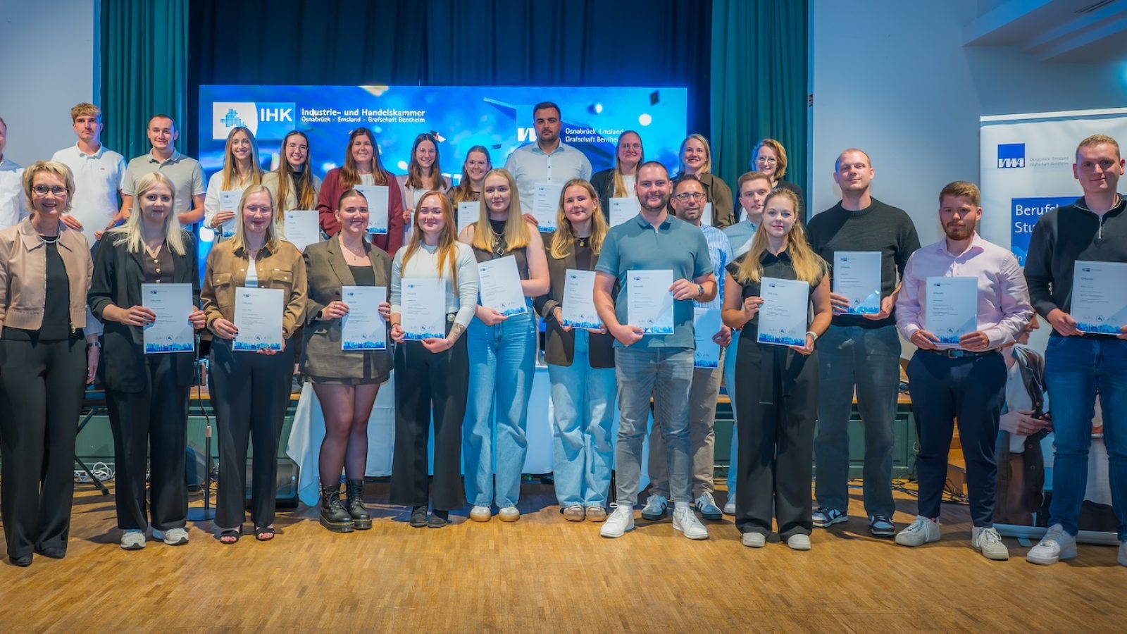 Gruppenfoto der Geprüften Wirtschaftsfachwirte mit ihren Urkunden vor der Bühne im Hofbräu an der Wilhelmshöhe in Lingen, links IHK-Vizepräsidentin Maria Borgmann
