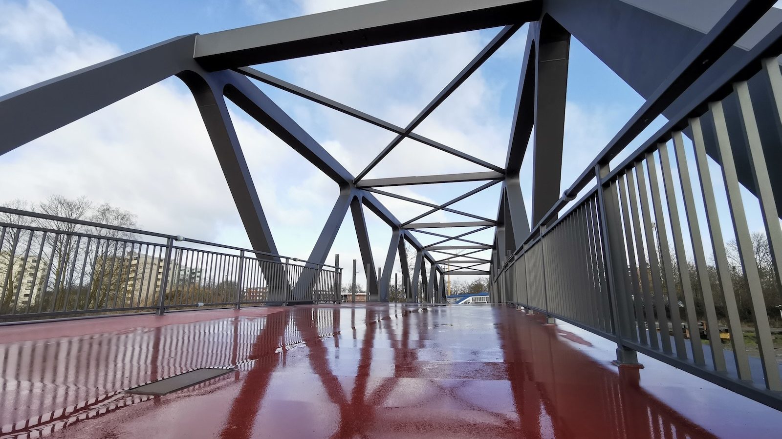 Blick über eine stählerne Fachwerkbrücke für Fußgänger und Radfahrer mit rotem Belag
