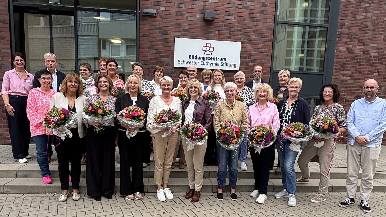 Gruppenfoto der geehrten Mitarbeiterinnen mit Blumensträußen vor dem Bildungszentrum Schwester Euthymia Stiftung