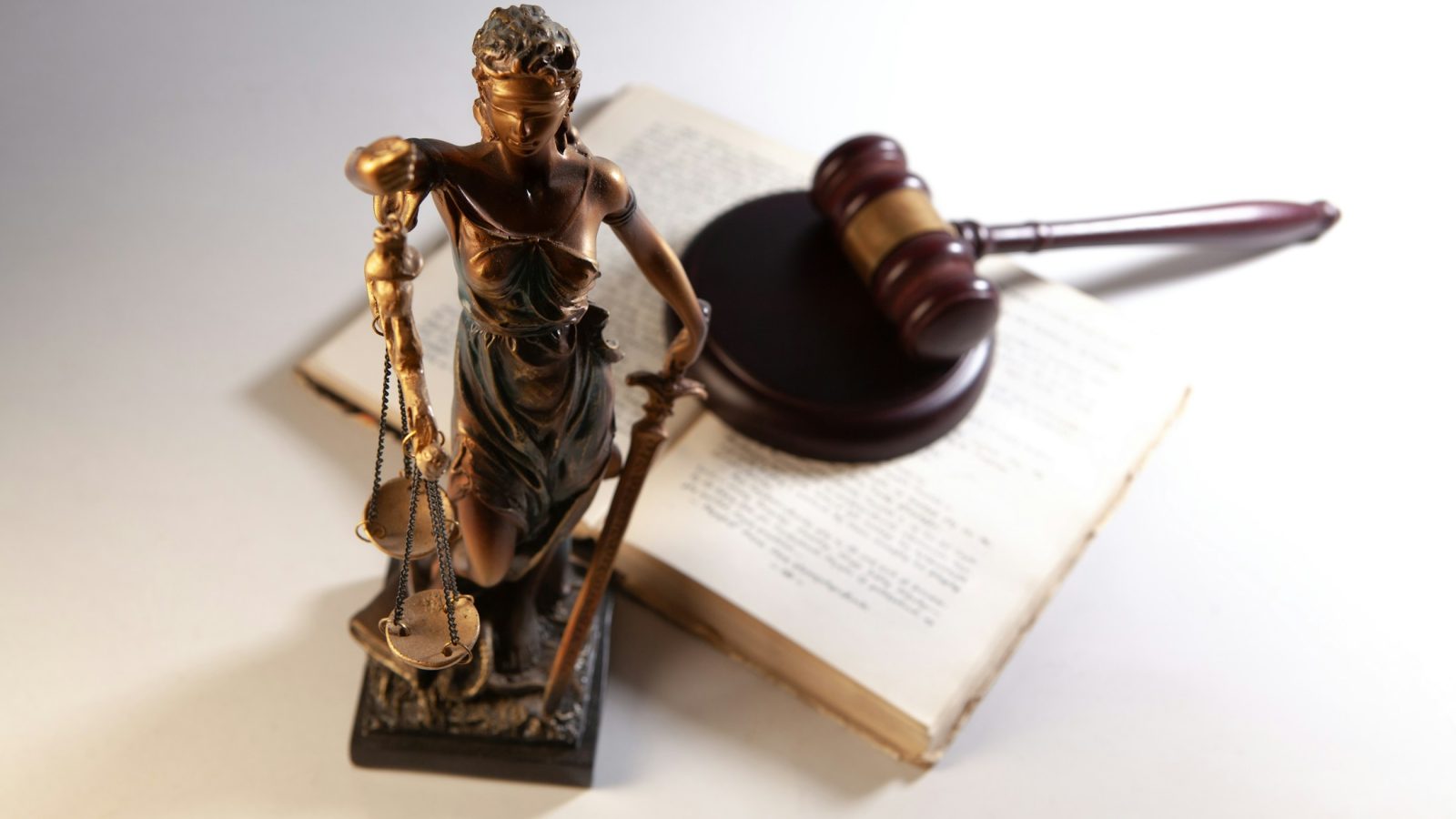 Justitia-Figur, Richterhammer und aufgeschlagene Gesetzbücher auf einem Schreibtisch