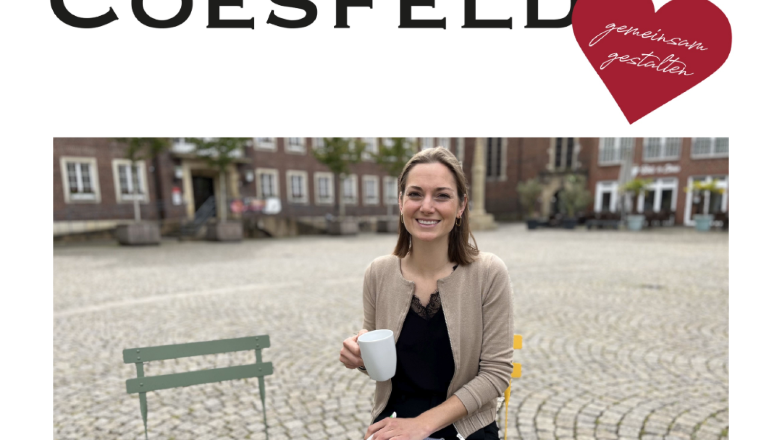 Frau mit einer Tasse Kaffee in der Hand, die auf einem Stuhl sitzt und in die Kamera lächelt.