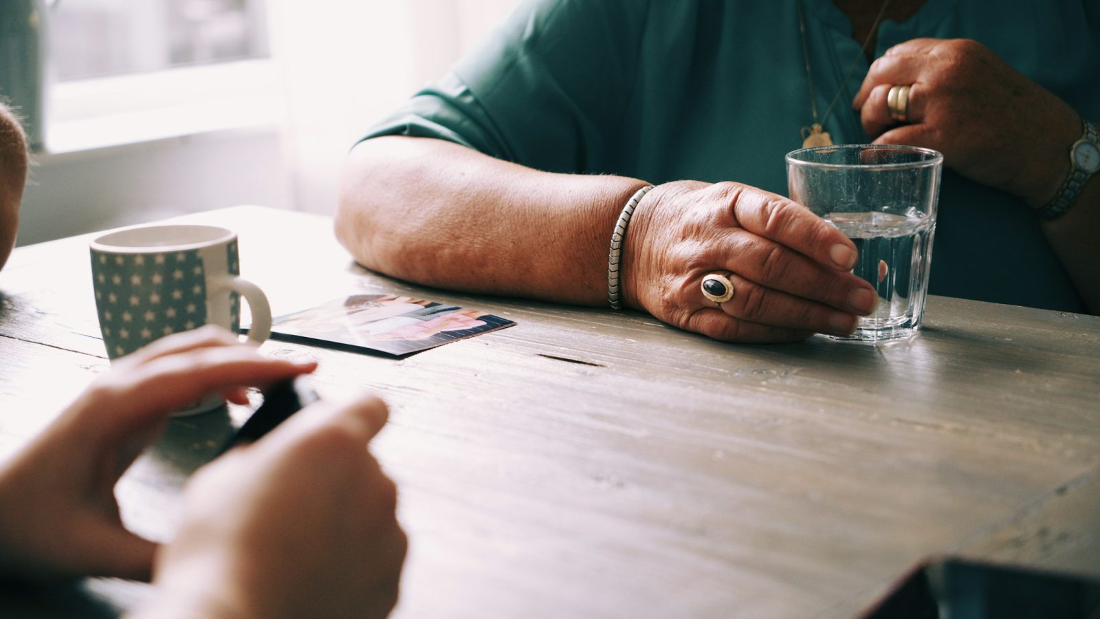Ältere Frau und Familie sitzen bei Kaffee zusammen am Tisch und unterhalten sich