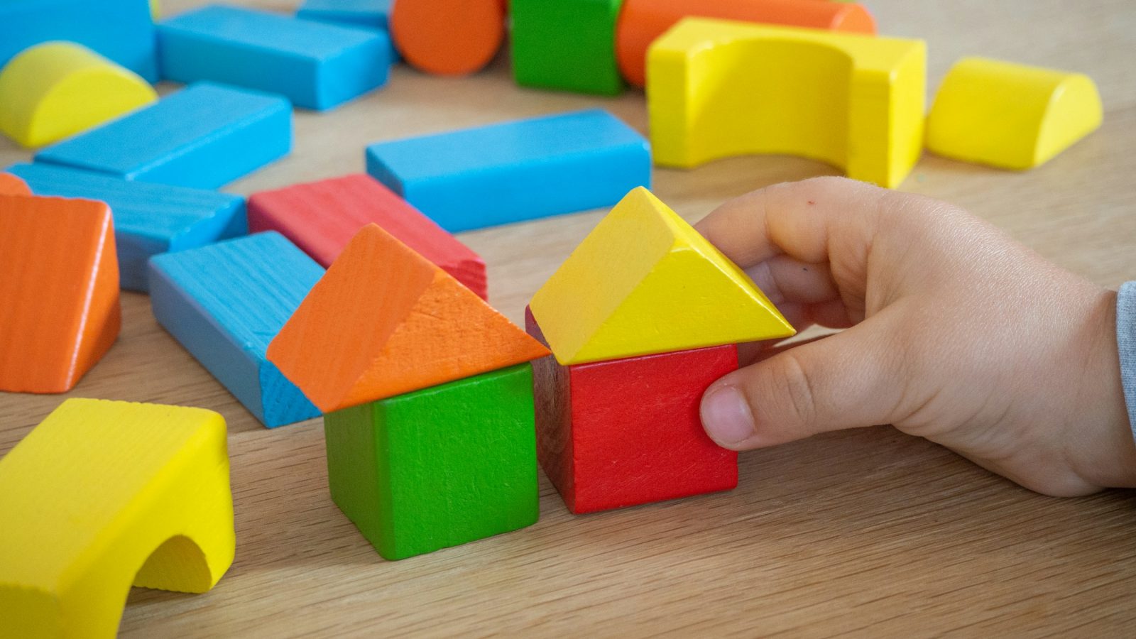 Kinderhand stapelt bunte Holzbausteine